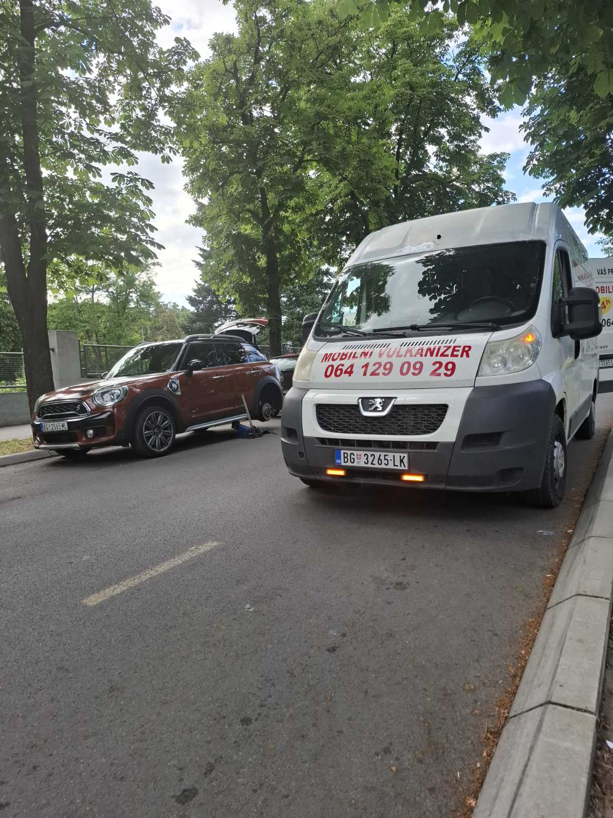 Beli Peugeot kombi mobilnog vulkanizera Milan parkiran pored smeđeg Mini Cooper Countrymana — zamena točka na terenu na ulici u Beogradu