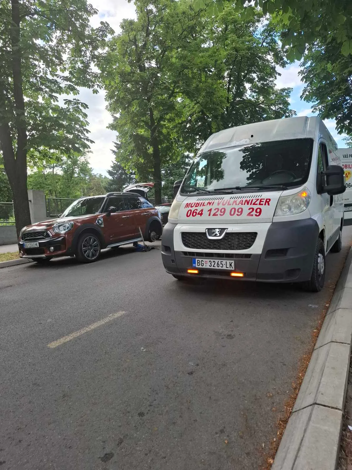 Beli Peugeot kombi mobilnog vulkanizera Milan parkiran pored smeđeg Mini Cooper Countrymana — zamena točka na terenu na ulici u Beogradu